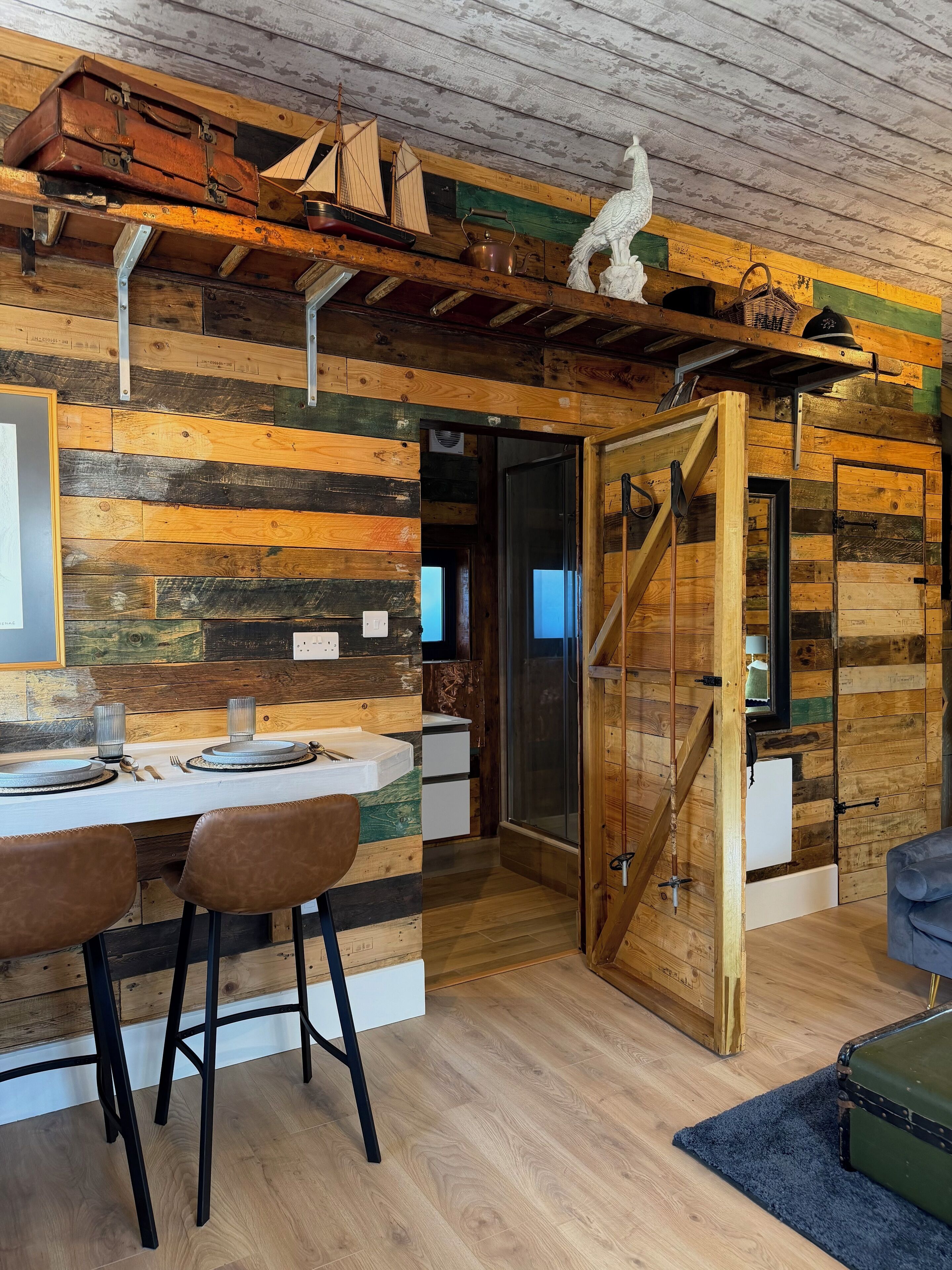 Un intérieur rustique en bois, avec un coin repas, une porte en bois et une petite maquette de bateau accrochée au mur.