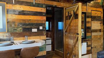 Un intérieur rustique en bois, avec un coin repas, une porte en bois et une petite maquette de bateau accrochée au mur.