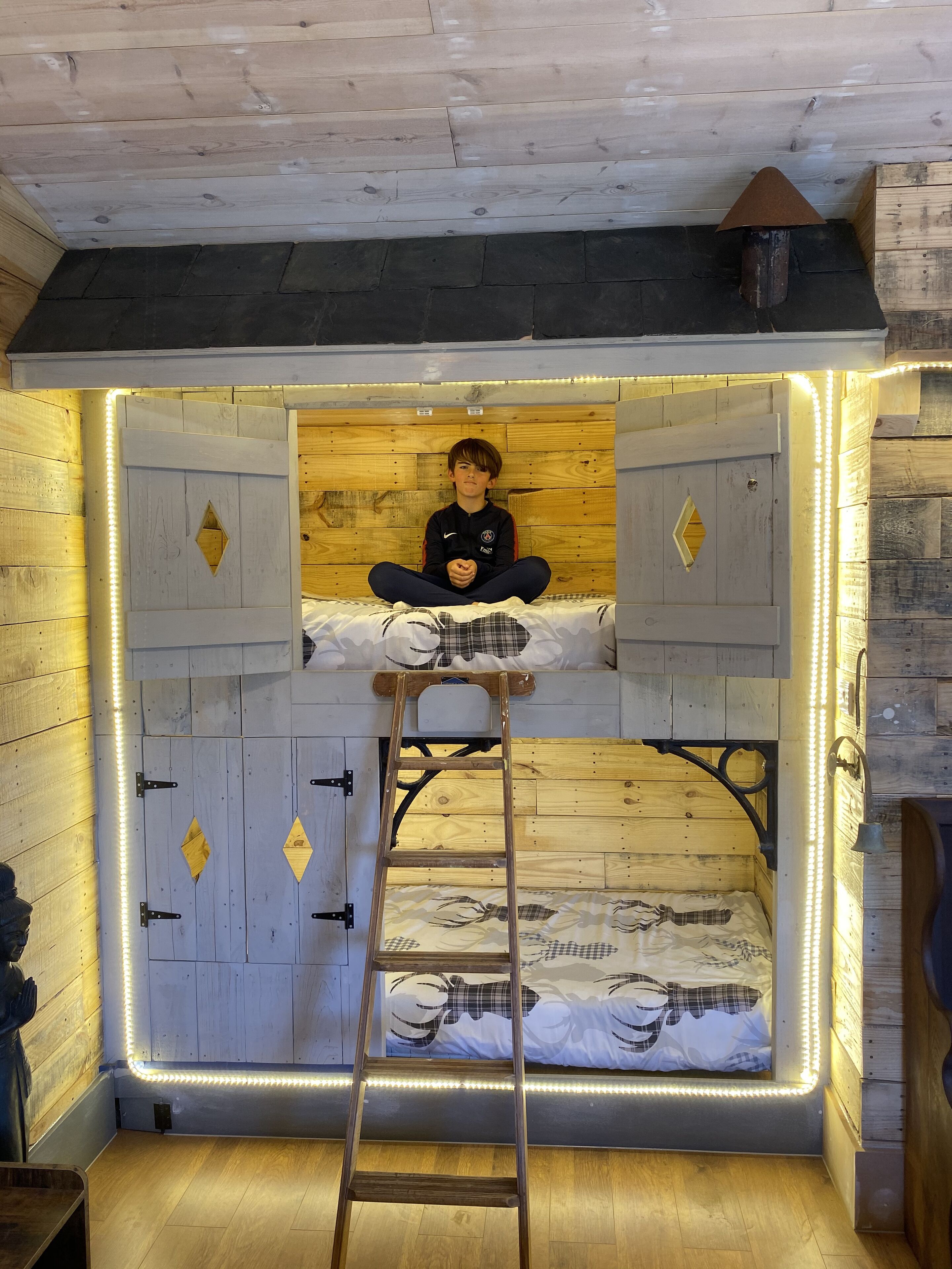 Een stapelbed met een ladder, houten wanden en LED-verlichting.