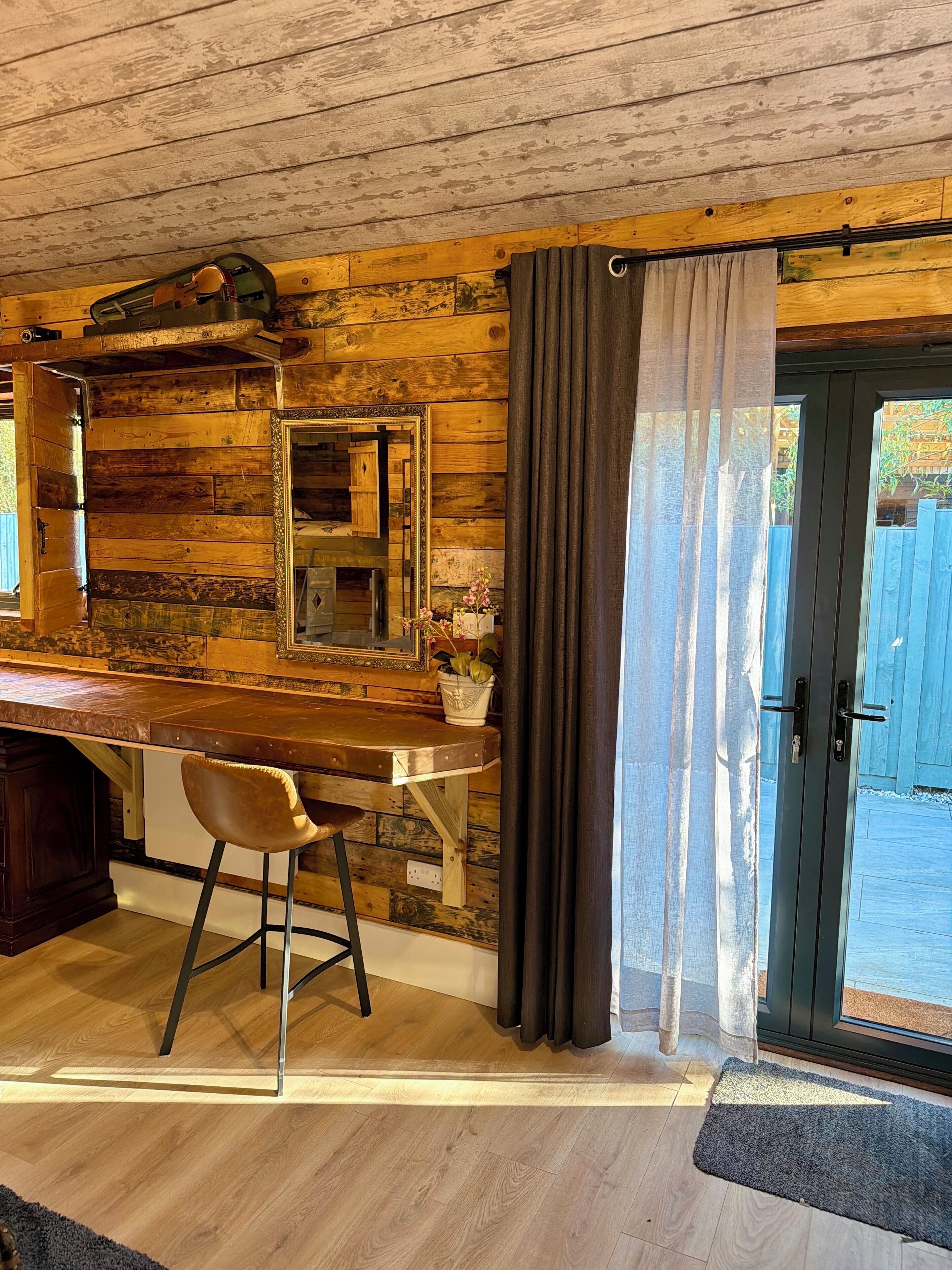 A rustic kitchen with a wooden interior, a bar counter, and a stool.