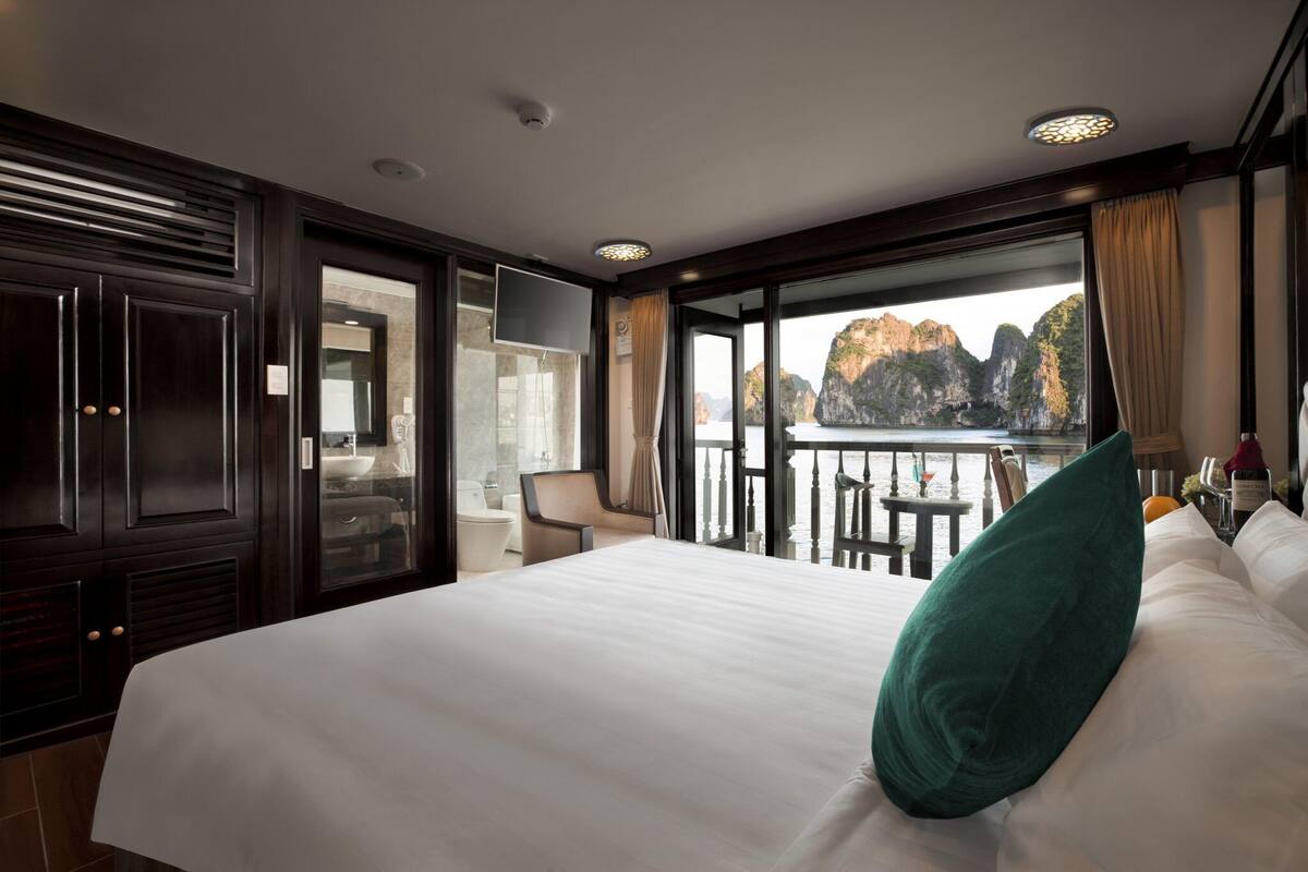 A hotel room with a large bed, a TV, a balcony with a view of cliffs, and a dining area.