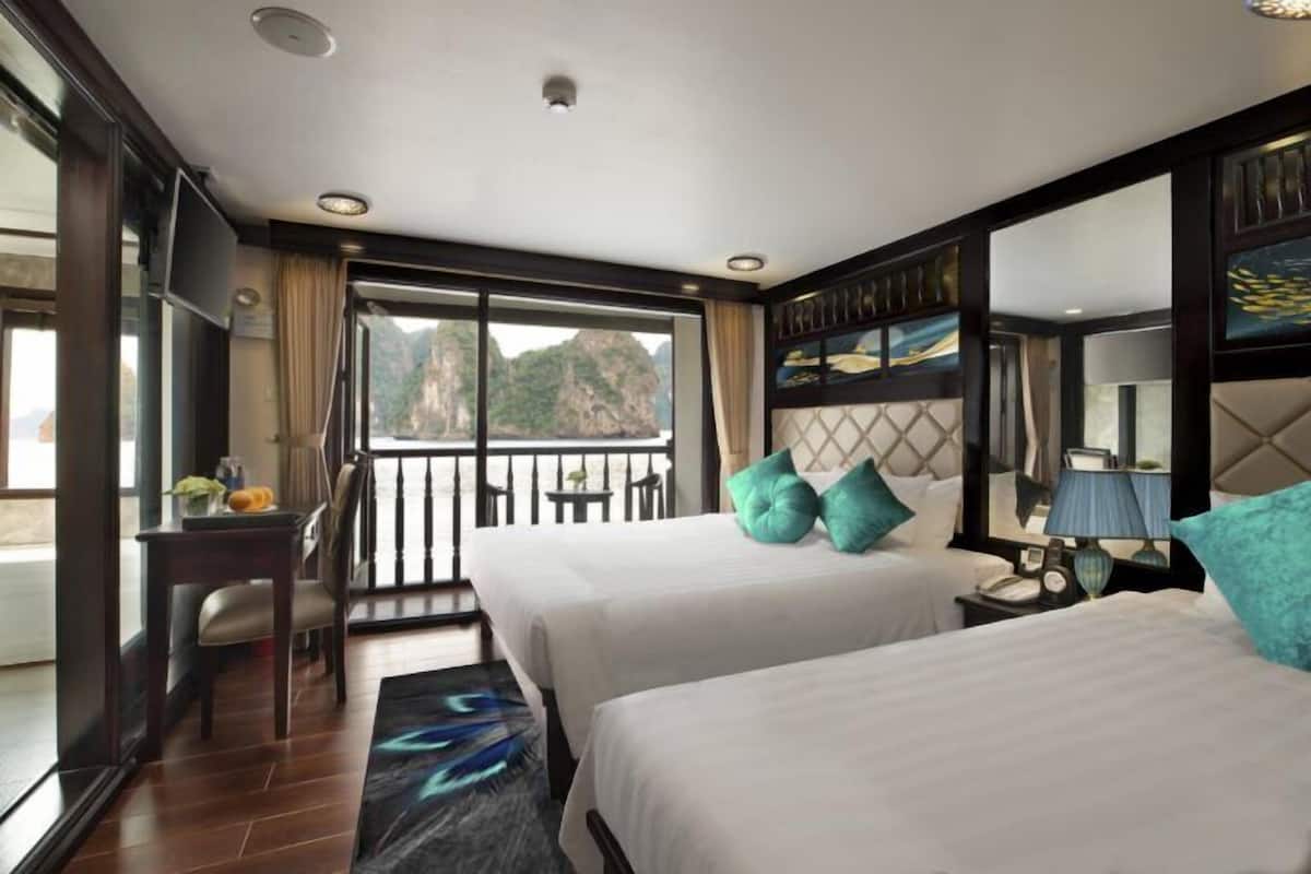A hotel room with two beds, a desk, and a balcony with a view of mountains.