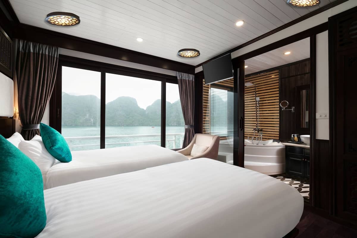 A modern hotel room with two beds, a large window with a view of mountains, a private bathroom, and a seating area with a view.