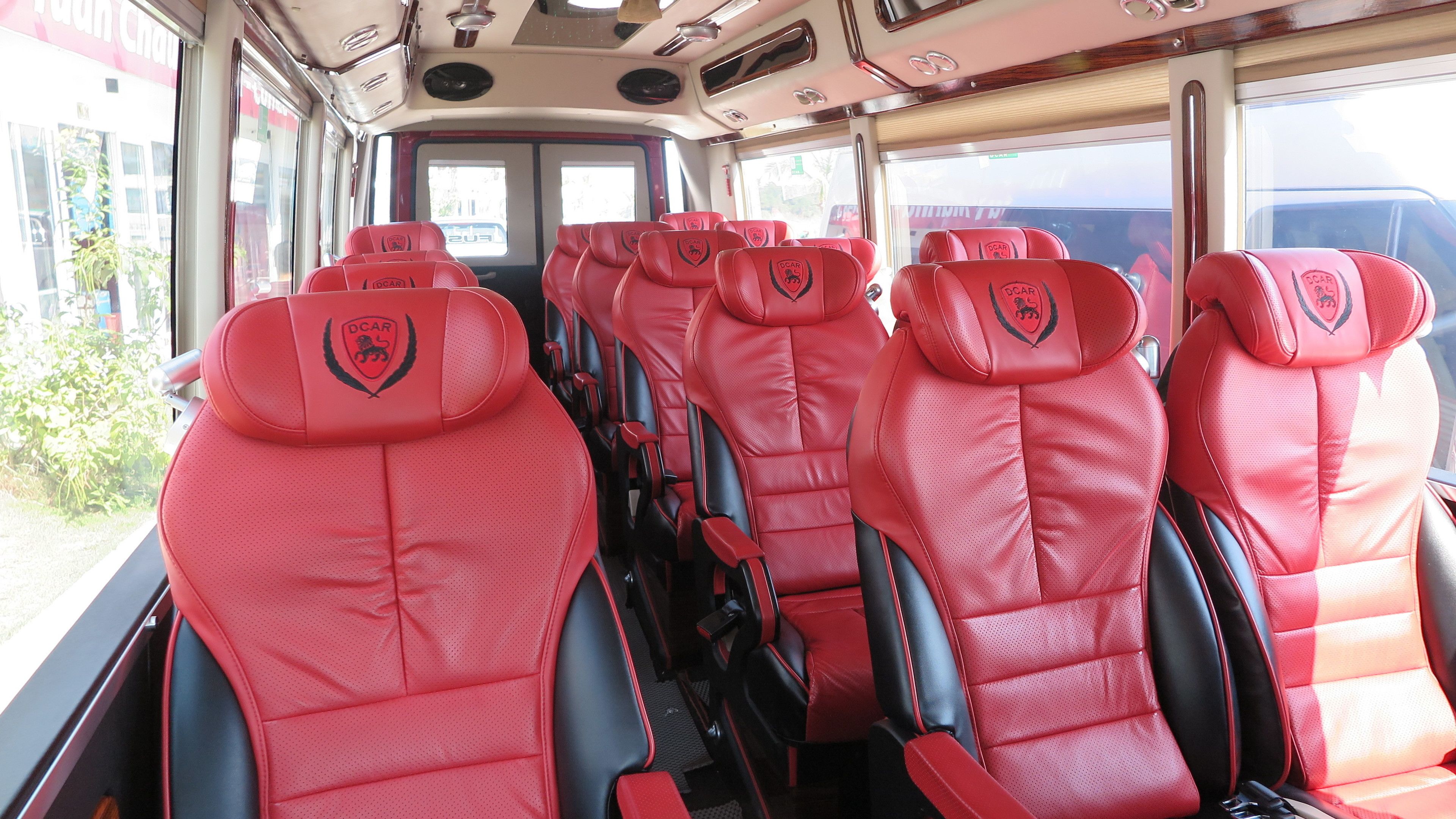 A bus interior with red leather seats featuring a logo, windows, and a view of the outside.