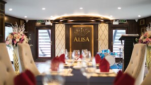 Een eetgedeelte met een gedekte tafel, een bord met de tekst 'ALISA' op de muur en twee vluchtwegborden boven de deur.