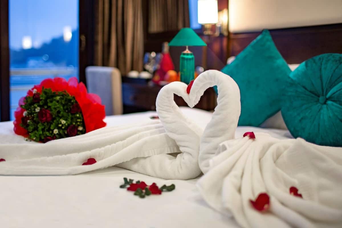 A bed with a heart-shaped towel arrangement, a bouquet of flowers, and teal pillows.