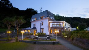 A large, white building with multiple windows and a well-lit entrance. - Oxwich Bay Hotel (Swansea)