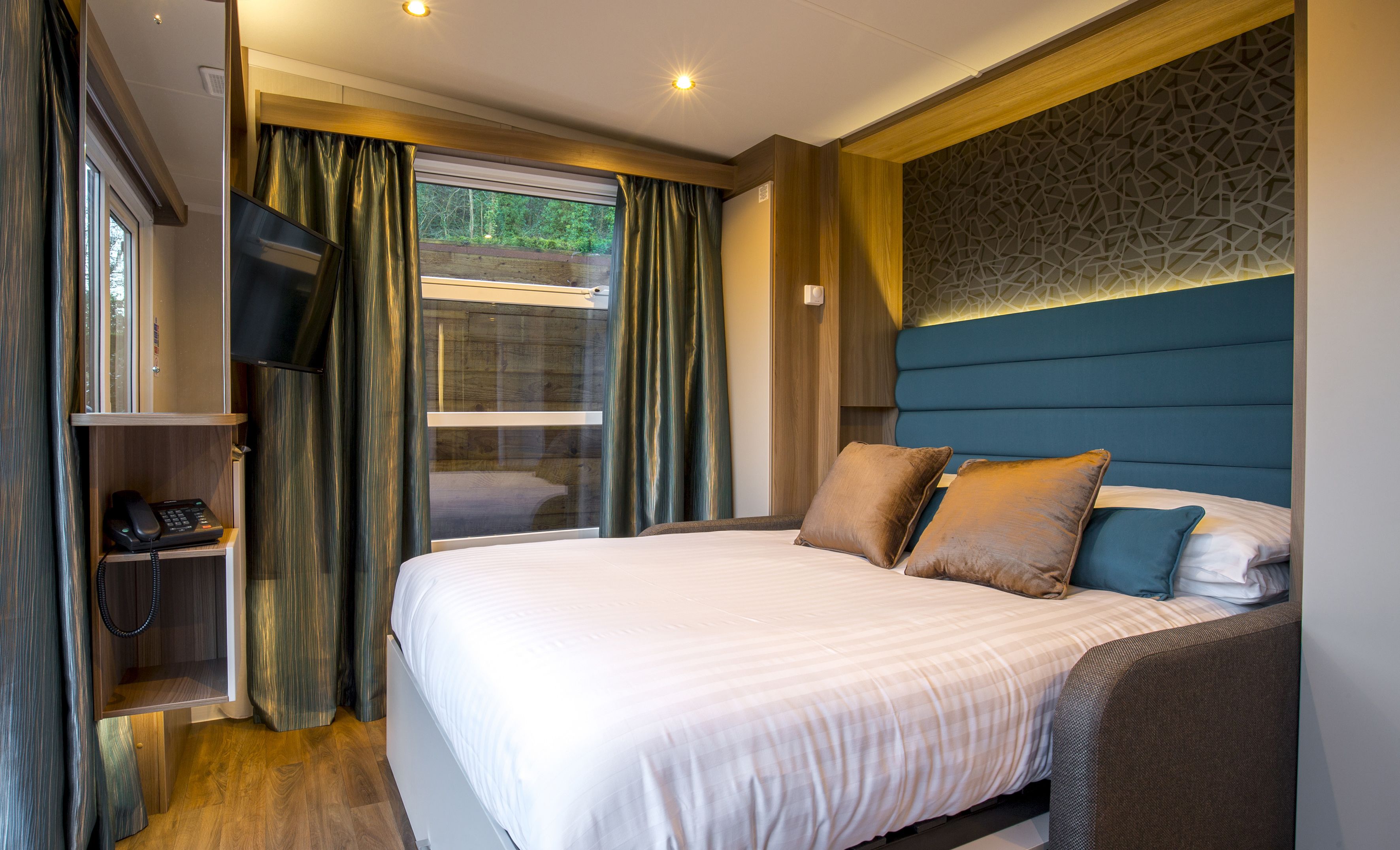 A modern hotel room with a large bed, a desk with a telephone, and a view of the outdoors through a window.