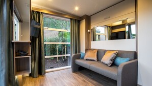 A modern living room with a sofa, a television, and a large window with curtains. - Oxwich Bay Hotel (Swansea)