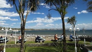 A beachside park with palm trees, picnic tables, and people sitting and walking. - Oxwich Bay Hotel (Swansea)