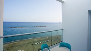 Un balcón con vistas despejadas al mar y a una playa de arena. Hay dos sillas y una mesa en el balcón.