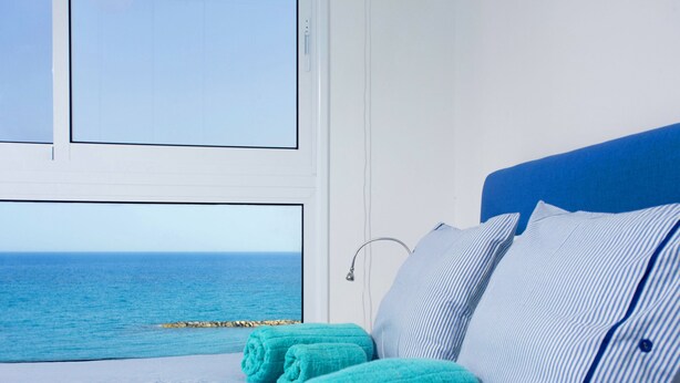 Una cama con toallas enrolladas, vista al mar y una ventana con persianas.