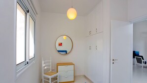 Un dormitorio con un armario blanco, un espejo redondo, un aparador de madera, una silla blanca y una alfombra azul.