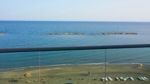 Vista de una playa desde un balcón, con cielo despejado, arena dorada y mar tranquilo.