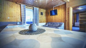 Una habitación con paneles de madera, una cama, un televisor montado en la pared y una ventana con cortinas.