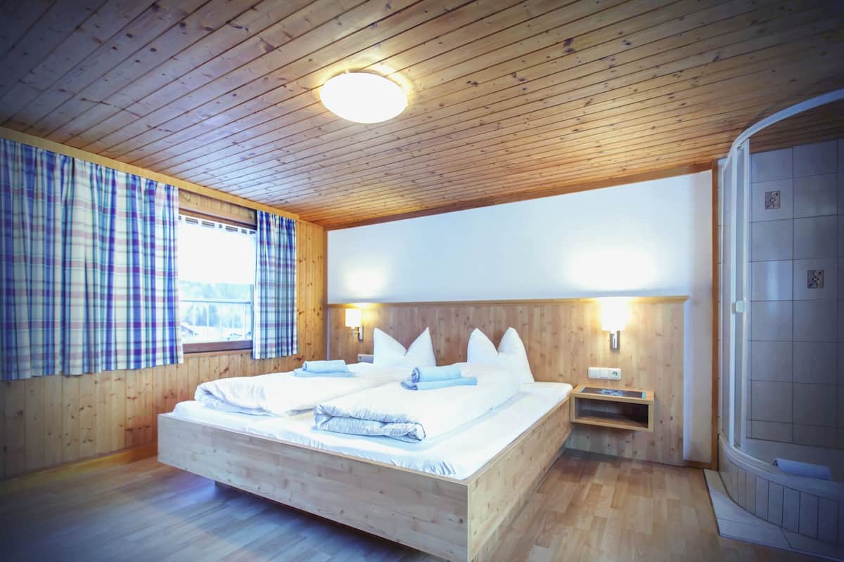 Un dormitorio con paneles de madera, una cama grande, dos mesitas de noche, un banco empotrado y una zona de ducha.