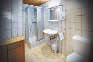 A bathroom with a shower, sink, toilet, and wooden cabinet.