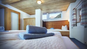 Un dormitorio con techo de madera, cama con ropa de cama blanca, toalla azul y ventana con vista a la montaña.