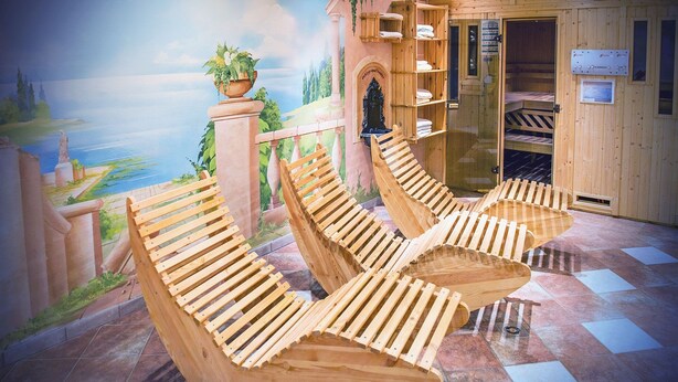 Una habitación con sillones de madera, un mural de un paisaje y una puerta de madera con repisas.