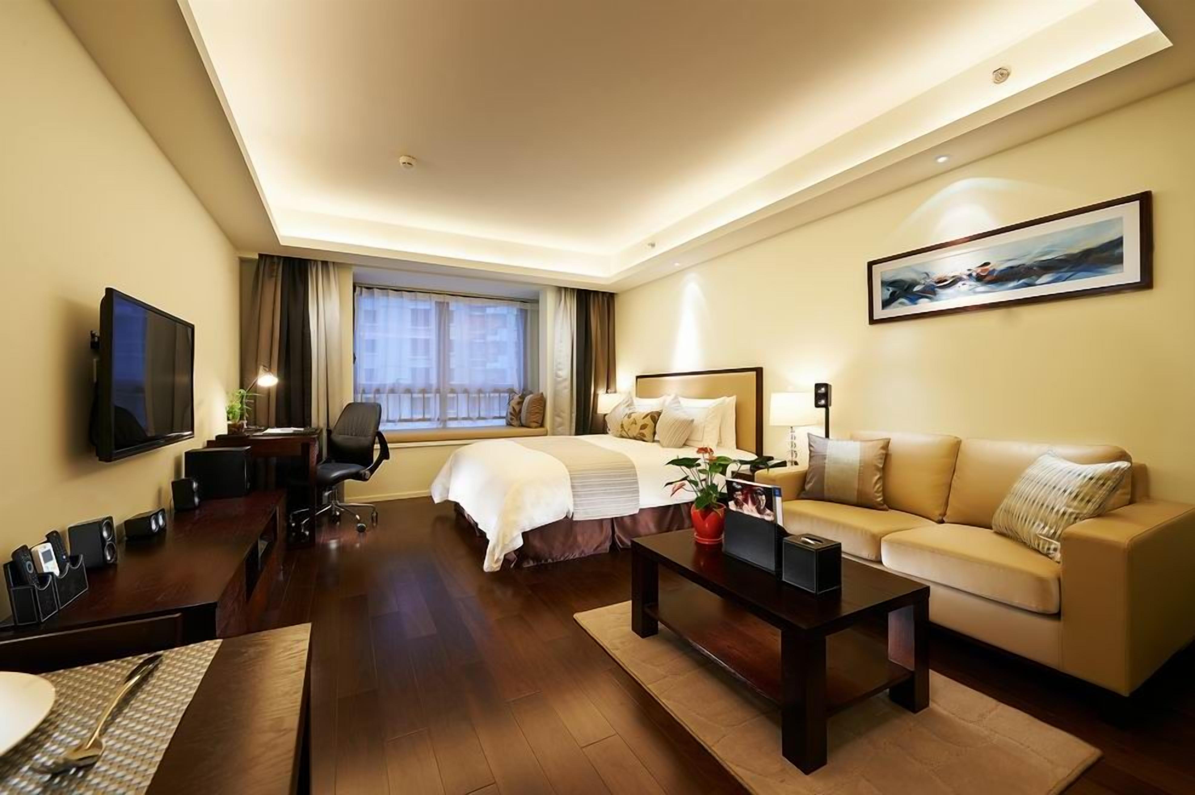 A hotel room with a bed, a sofa, a TV, a desk with a chair, and a dining table.