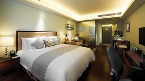 Habitación de hotel con una cama grande, mesita de noche, lámpara y un área de descanso con sofá y sillón.