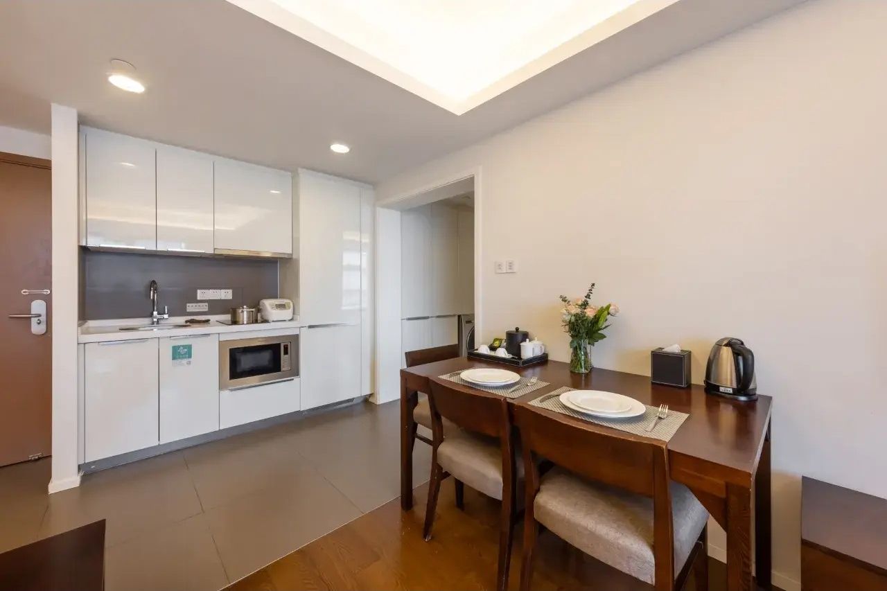 A modern kitchen with white cabinets, a microwave, and a dining table set with plates and cutlery.