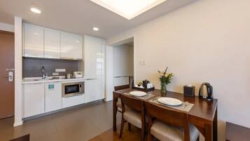 A modern kitchen with white cabinets, a microwave, and a dining table set with plates and cutlery.