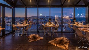 A restaurant with a panoramic city view, modern furniture, and fur rugs on the floor. - Breidablikk Gjestehus (Narvik)