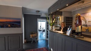 A reception area with a desk, a chair, a rug, a painting, and a statue. - Breidablikk Gjestehus (Narvik)