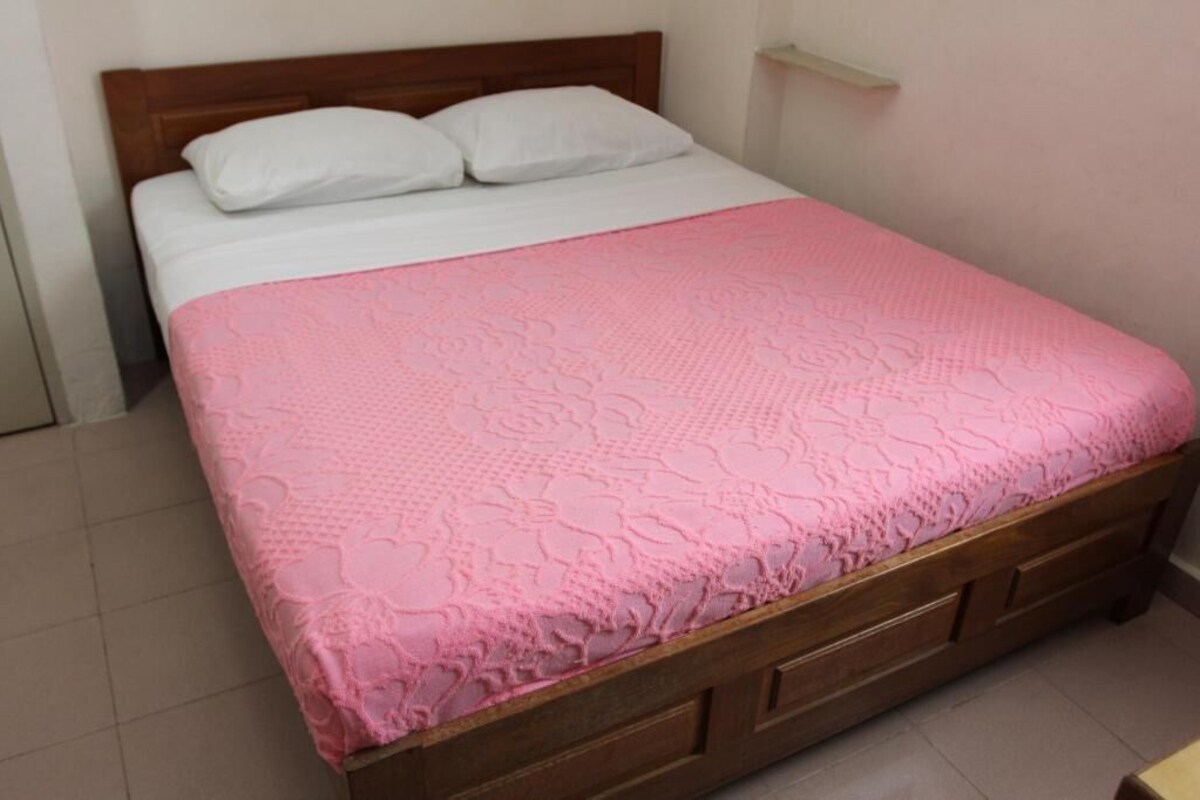 Ein Einzelbett mit Holzrahmen, weißer Bettwäsche und einer rosa, strukturierten Decke.