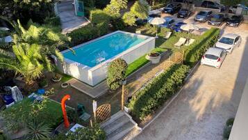 Une vue aérienne d’un hôtel doté d’une piscine, entouré d’une végétation luxuriante, et d’un parking où sont stationnées plusieurs voitures.