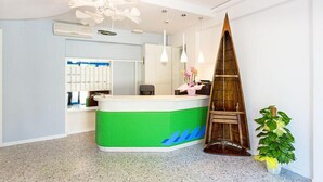A reception area with a green and white counter, a wooden sculpture, and a potted plant. - Hotel Costa Verde (Rosignano Marittimo)