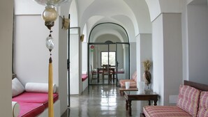 A spacious room with a high arched ceiling, a seating area with a pink sofa and a wooden table, and a dining area with a glass door. - Zubebi Resort (Pantelleria)