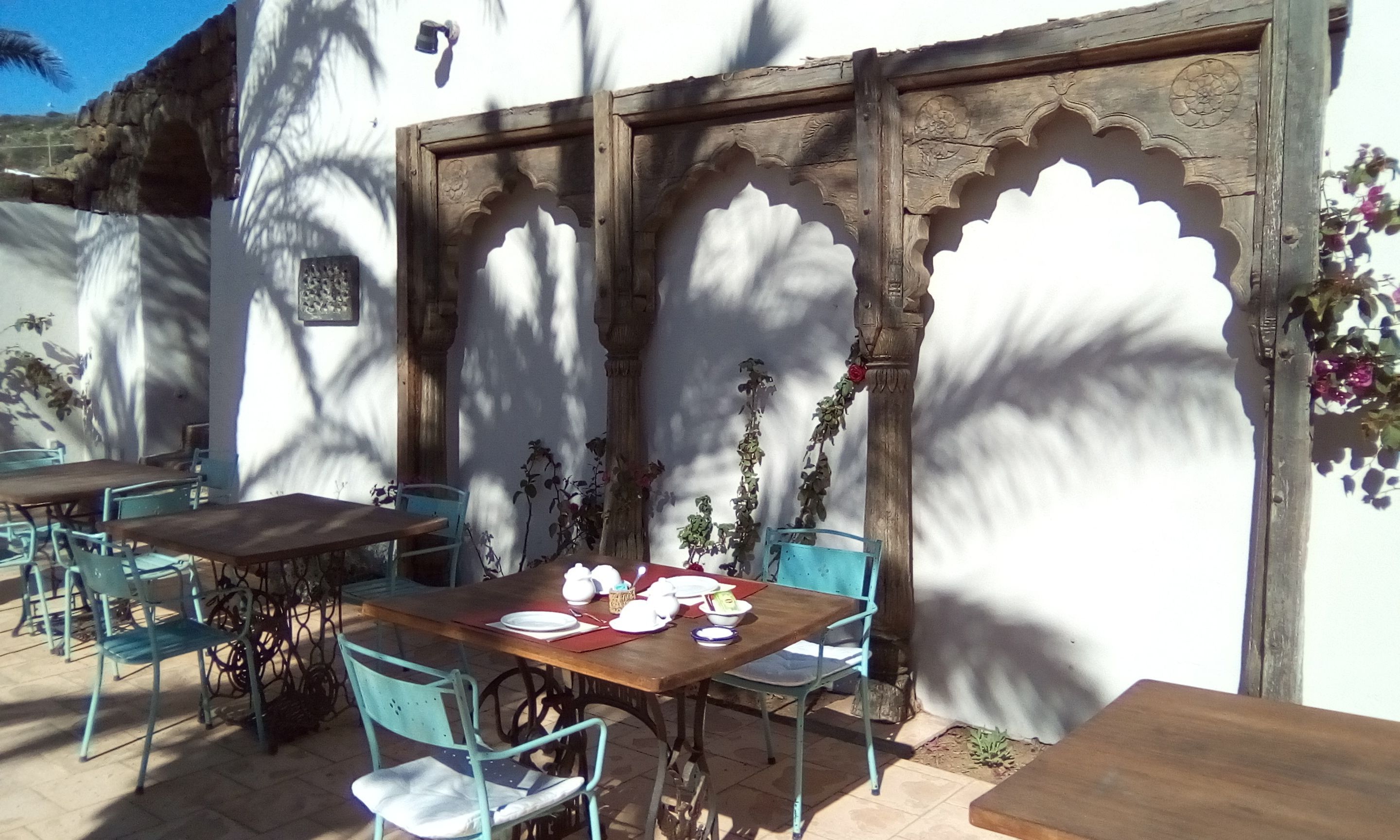 An outdoor dining area with a wooden table and chairs, surrounded by white walls with decorative arches.