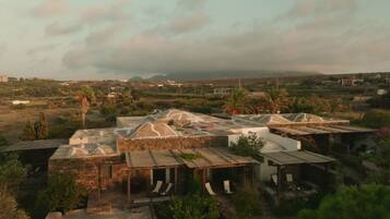 A rustic village with stone buildings and thatched-roof huts, surrounded by greenery and distant mountains.