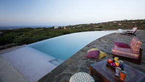 A poolside area with lounge chairs, a table with drinks, and a scenic view of the coastline. - Zubebi Resort (Pantelleria)