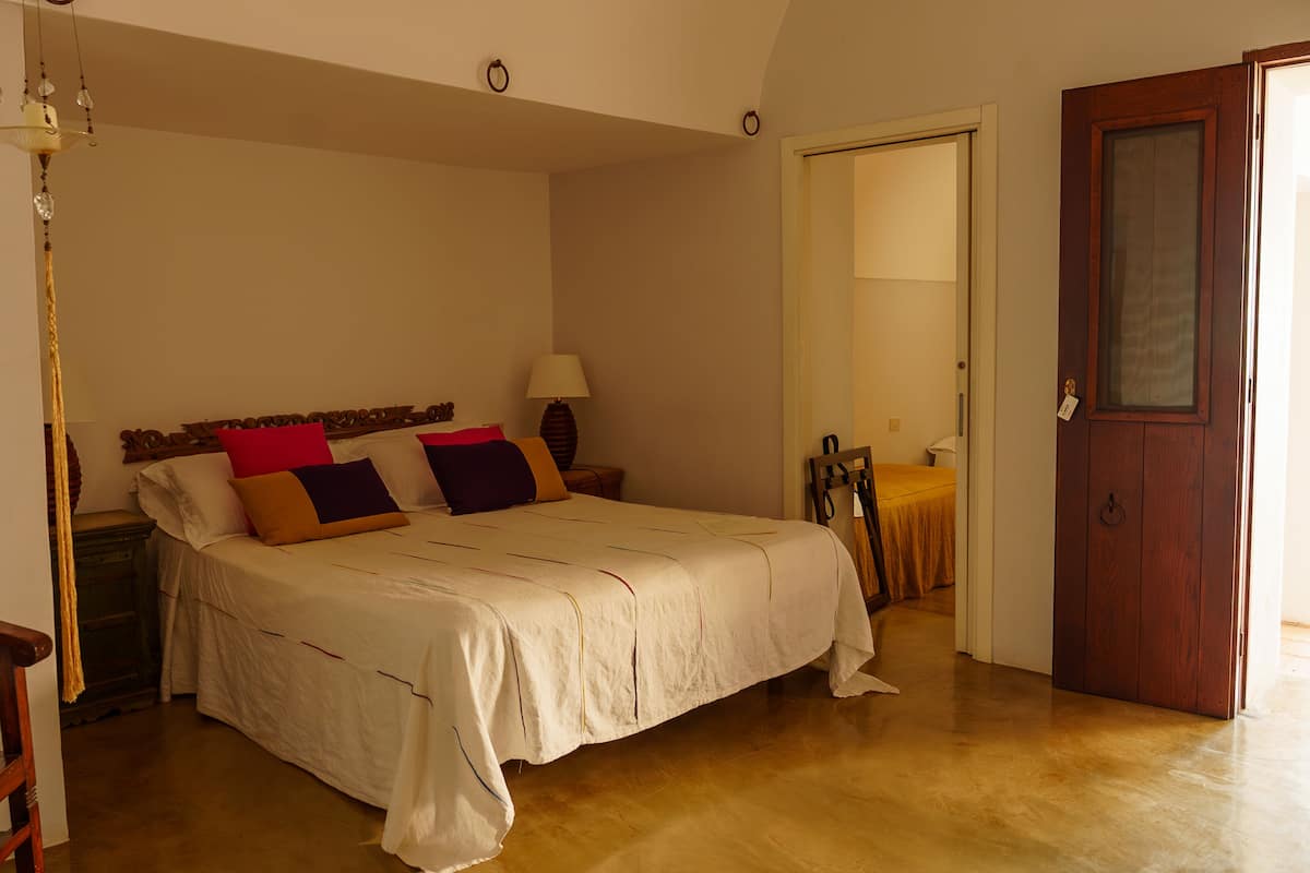 A bedroom with a bed, a wooden chair, a nightstand, a lamp, and a door.