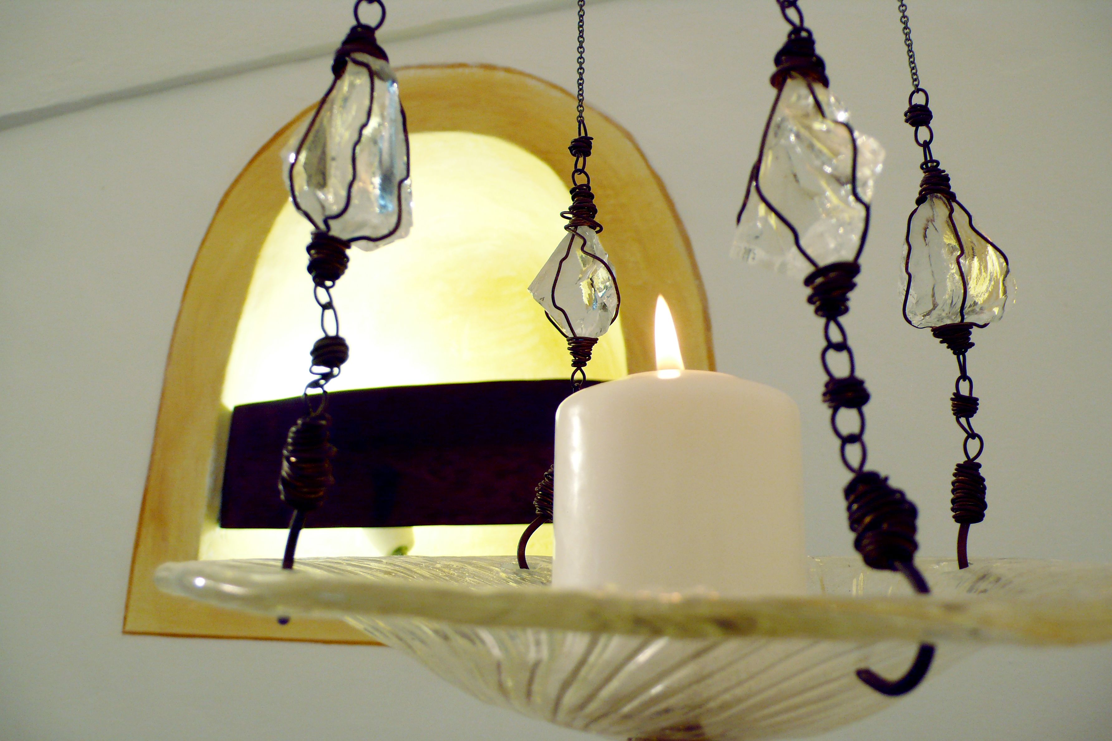 A candle on a white stand with a clear glass bowl, a white candle, and a window with an arched frame.