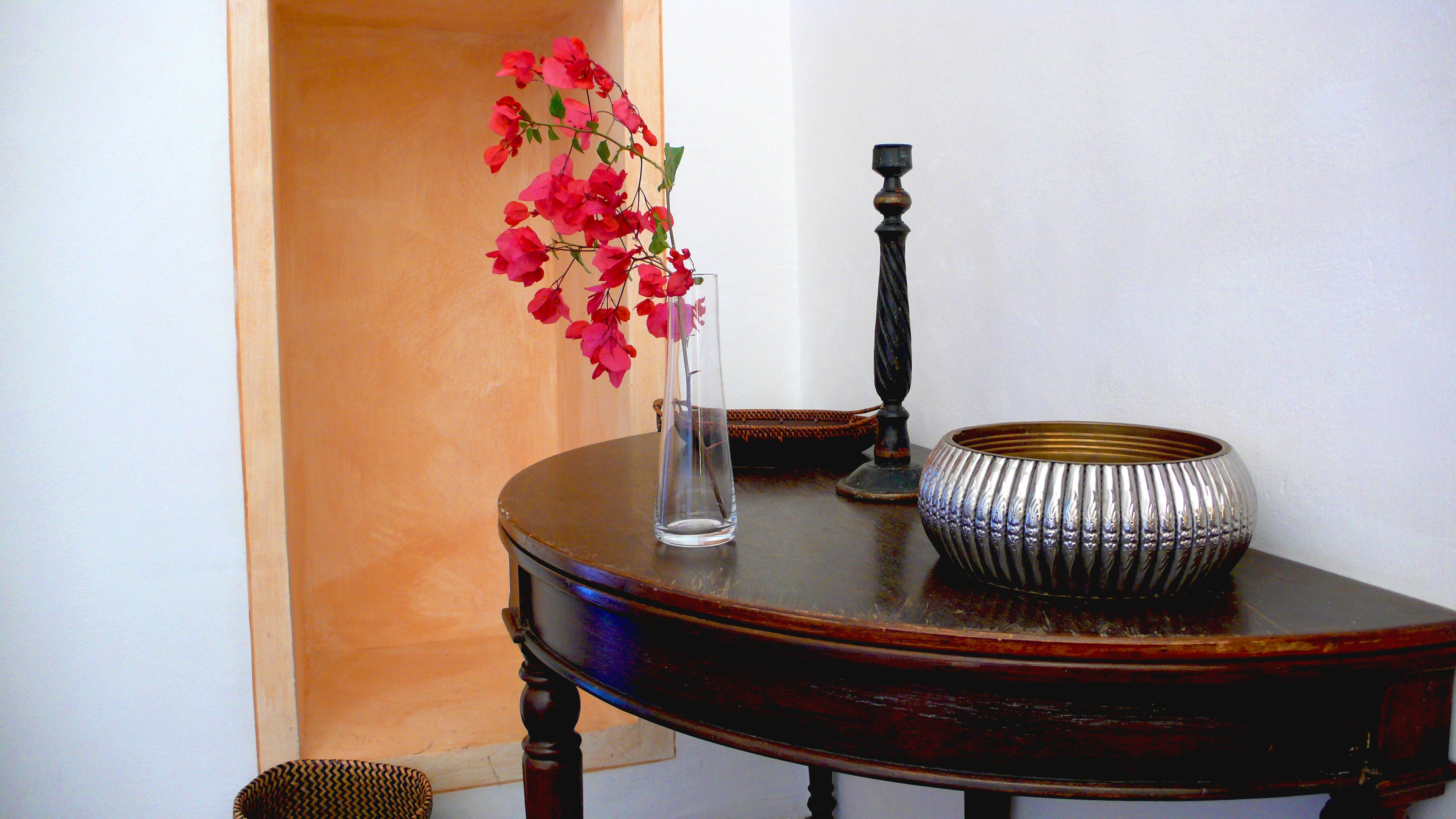 Una mesa de madera con un jarrón transparente que contiene flores rosas, un cuenco decorativo de metal y un candelabro.