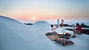 A group of people relaxing on a white, sloped surface with a sunset in the background. - Zubebi Resort (Pantelleria)