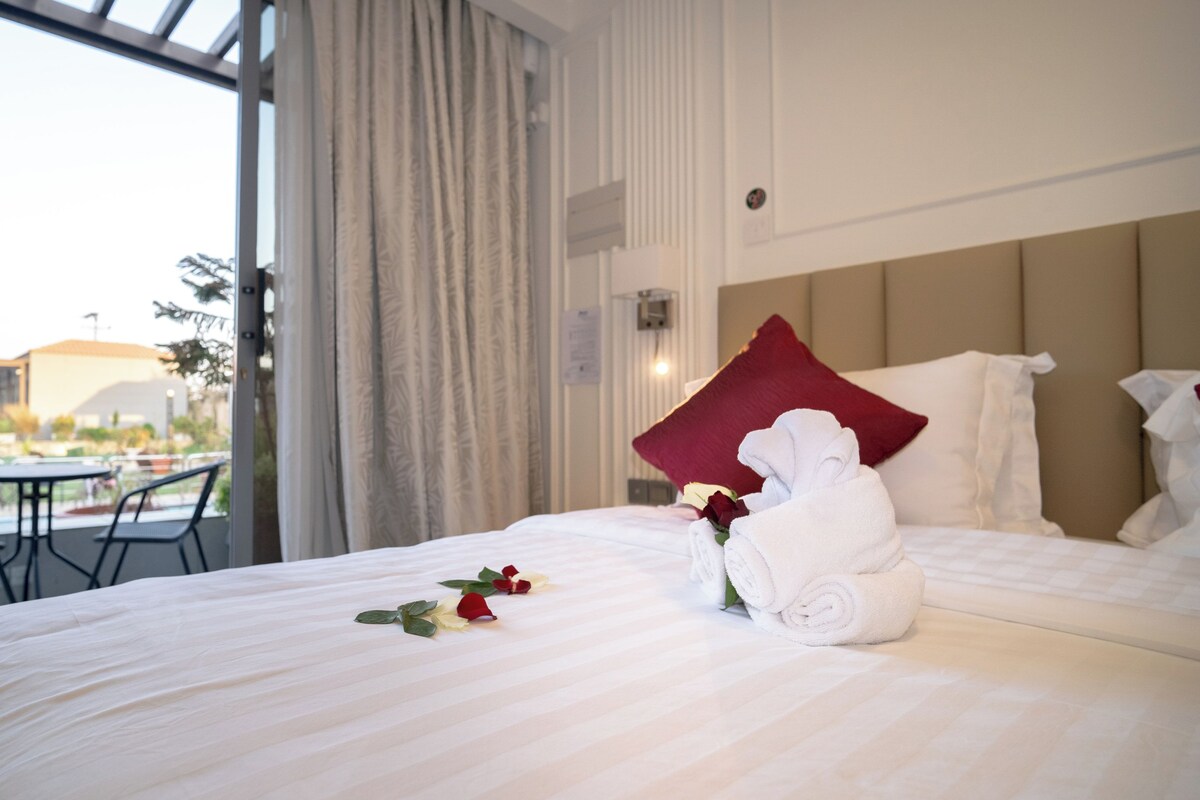 A hotel room with a bed, a red pillow, a white towel, and a rose.