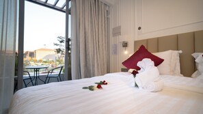 A hotel room with a bed, a red pillow, a white towel, and a rose.