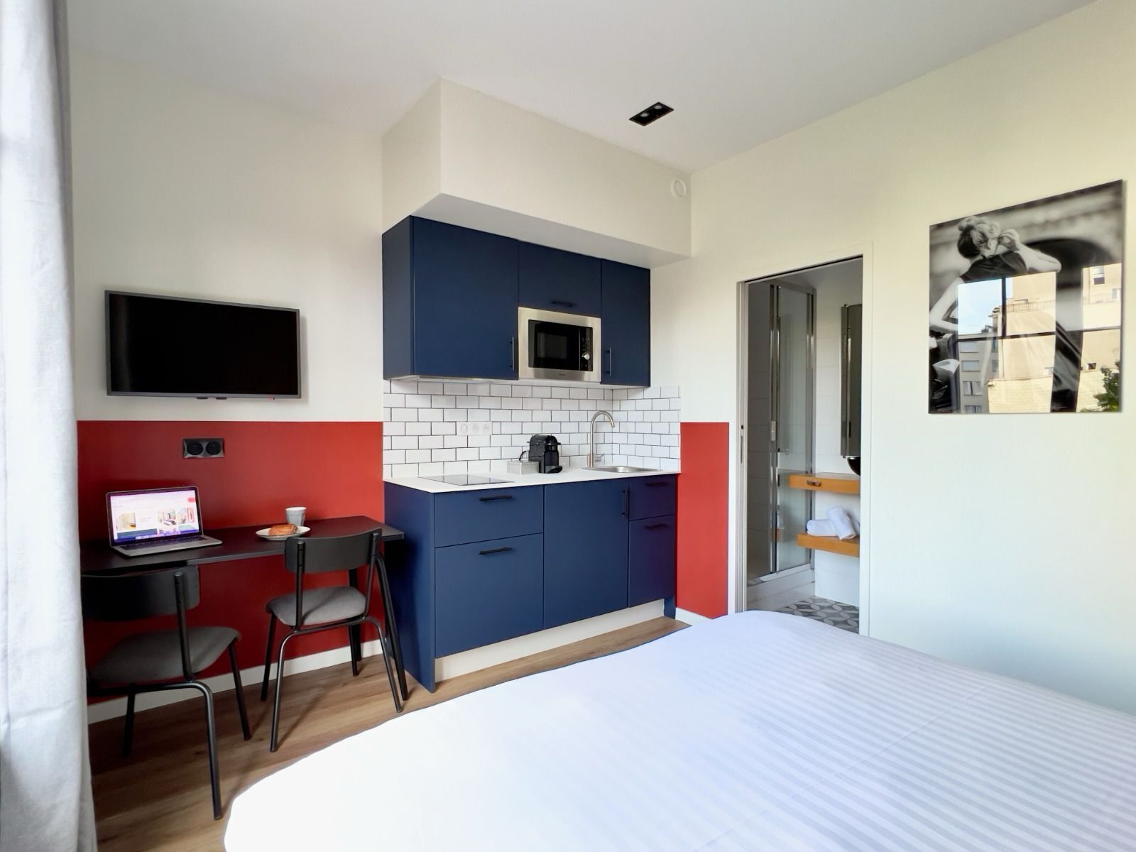 Een moderne hotelkamer met een bed, een bureau met een laptop, een magnetron en een televisie.