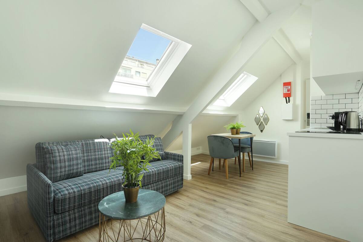 A modern apartment with a loft-style ceiling, a sofa, a dining area, and a kitchen.