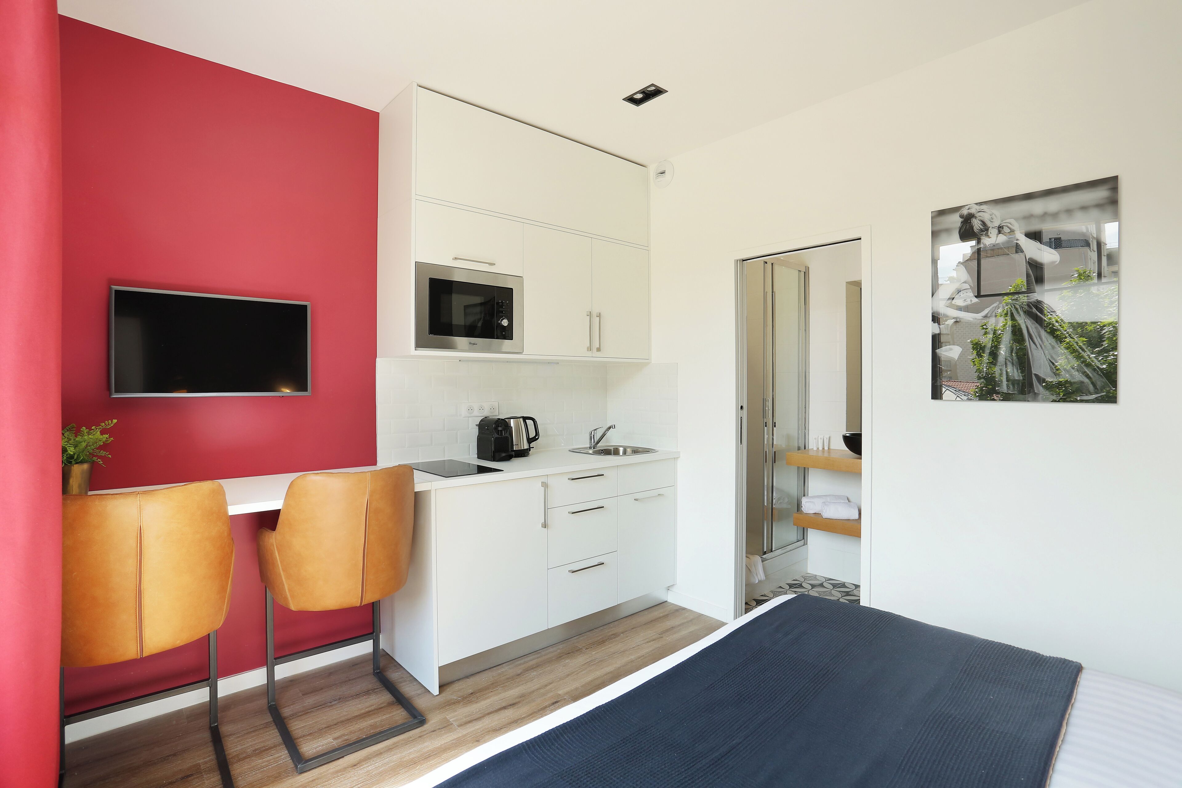 Ein modernes Zimmer mit roter Akzentwand, einem Flachbildfernseher, einer Mikrowelle, einem Waschbecken und einem Bett.