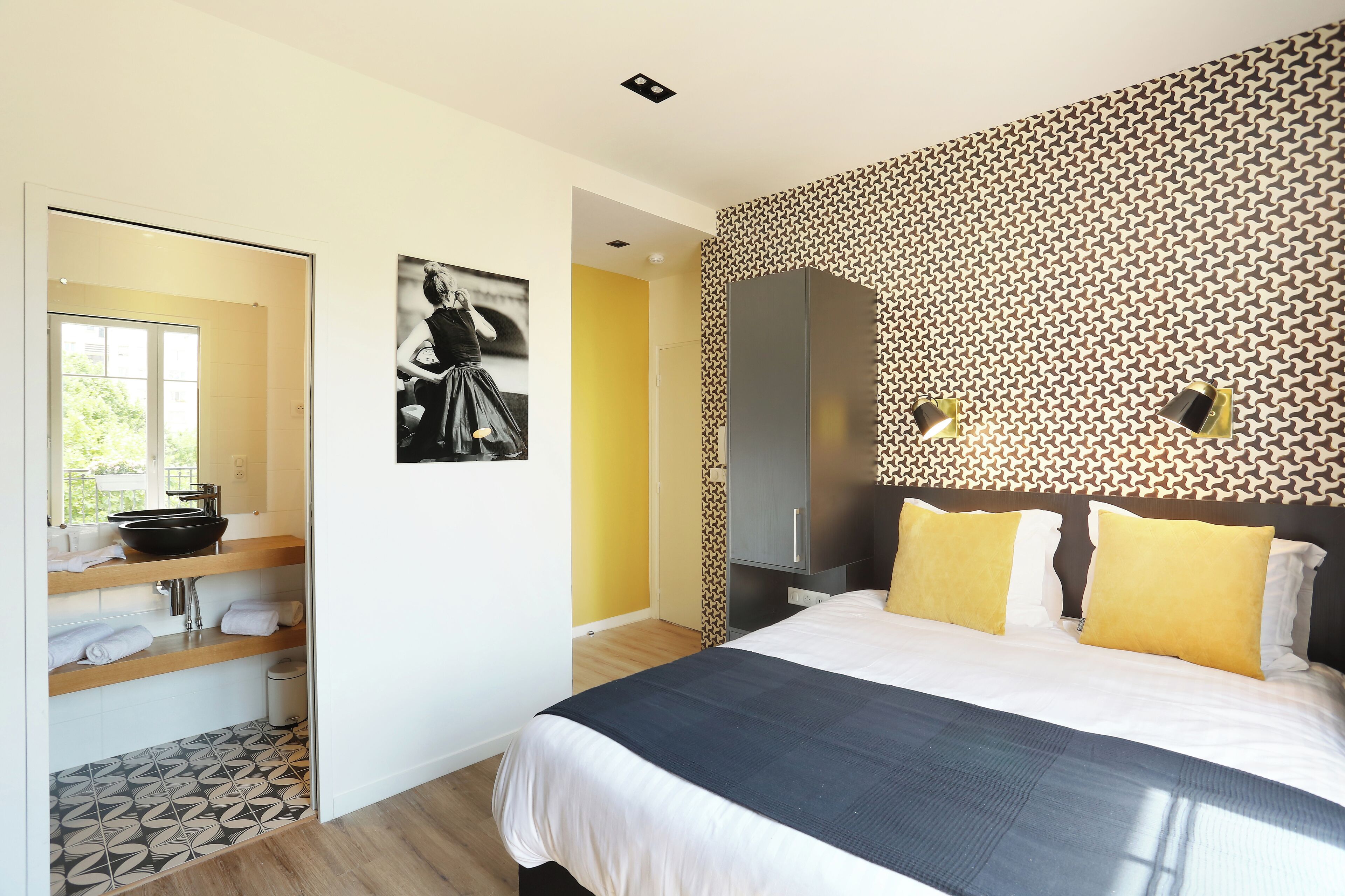 A modern bedroom with a bed, a vanity with a mirror, and a patterned wall.