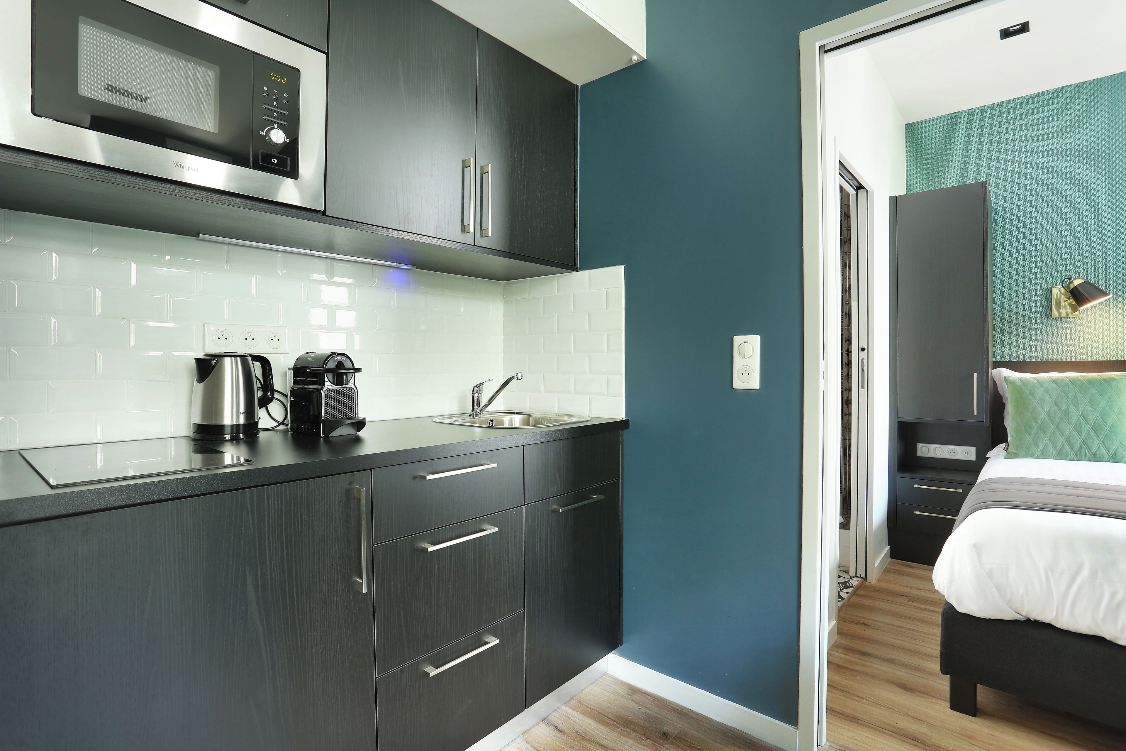 A modern kitchen with dark cabinetry, a stainless steel microwave, and a kettle.