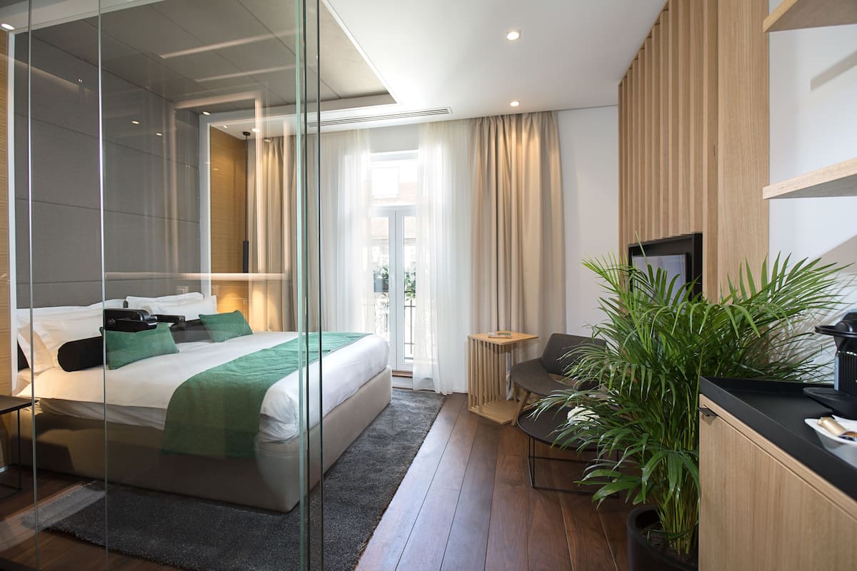 A modern hotel room with a large bed, a desk, a chair, a television, and a potted plant.