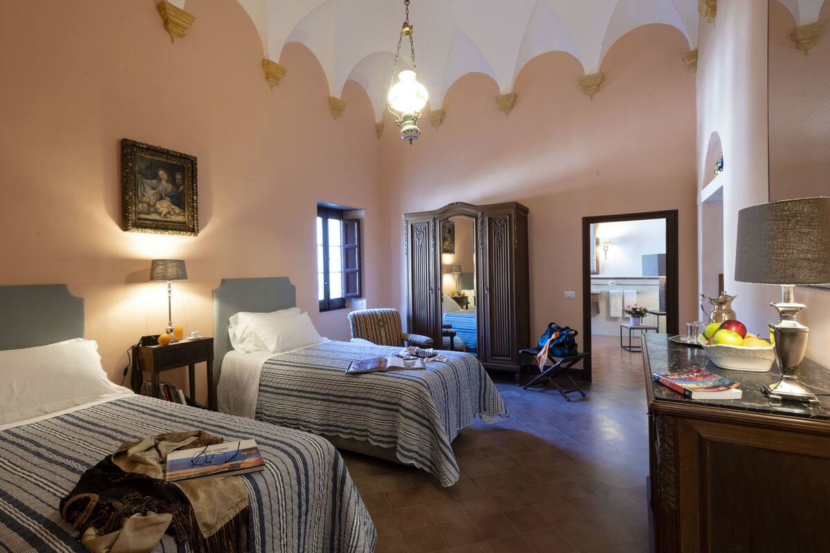 A hotel room with two beds, a wardrobe, a desk with a lamp, and a view of the hallway.