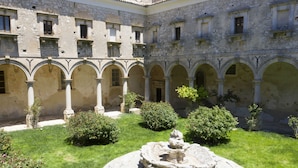 A courtyard with a central fountain, surrounded by stone arches and greenery.
